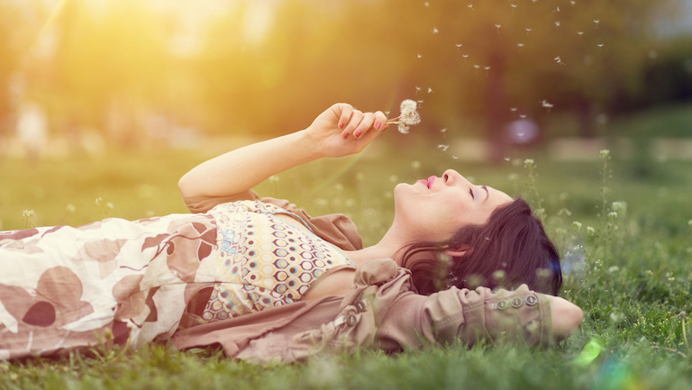 Young woman lying down in the grass and blowing dandelion